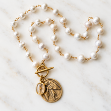 Load image into Gallery viewer, A mustard seed jewelry pearl and gold necklace featuring white freshwater pearls linked by gold chains, with a gold toggle clasp and a round gold medallion pendant depicting an angel and a mustard seed pendant.