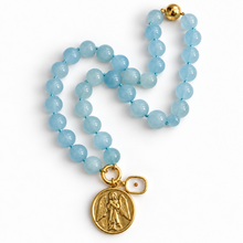 Load image into Gallery viewer, Mustard seed jewelry beaded necklace featuring light blue round beads and gold-tone metal accents, including a round medallion charm with an angel  and a small mustard seed charm.
